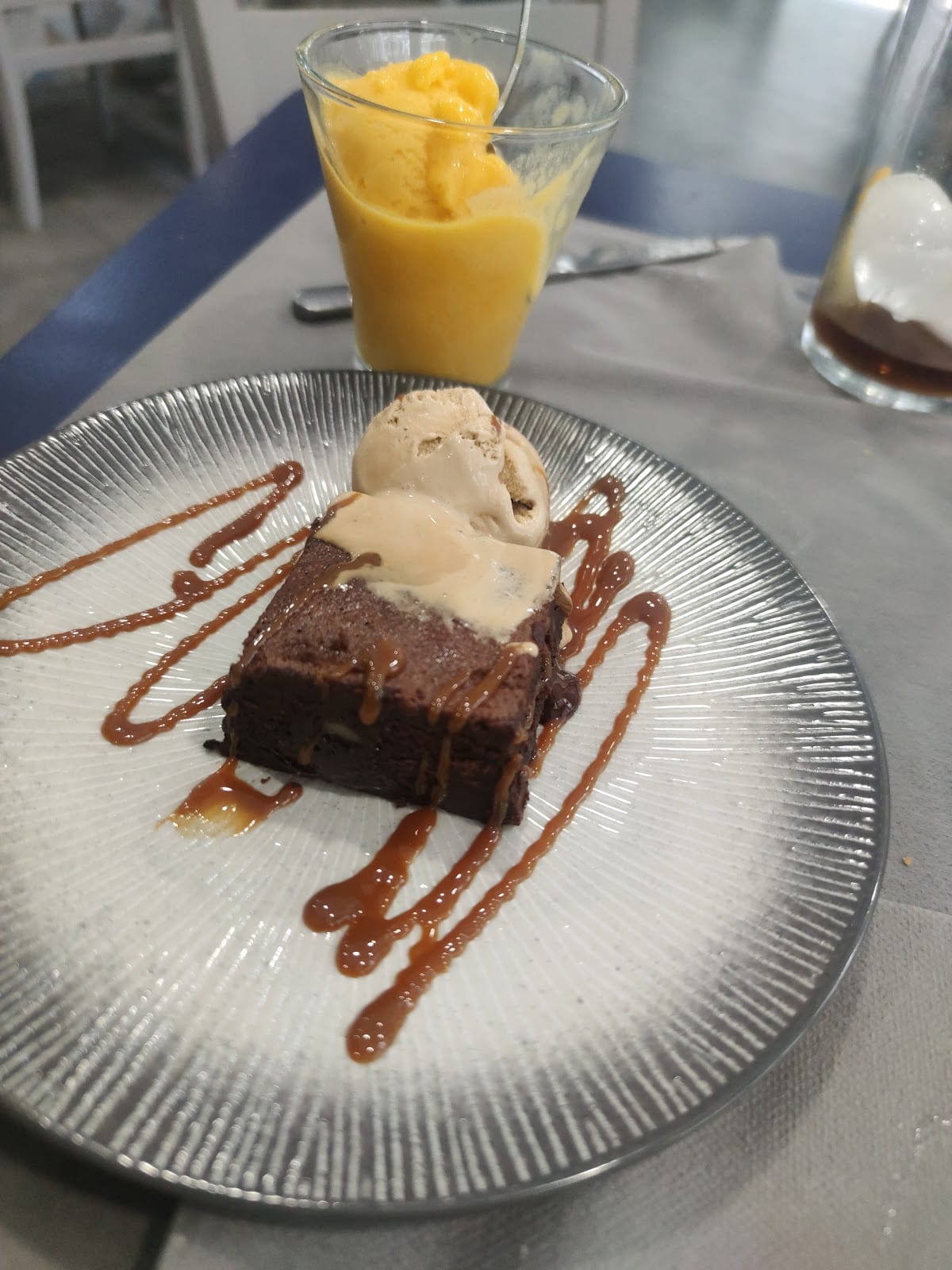 Brownie de chocolate con helado y caramelo, con un vaso de sorbete de mango al fondo