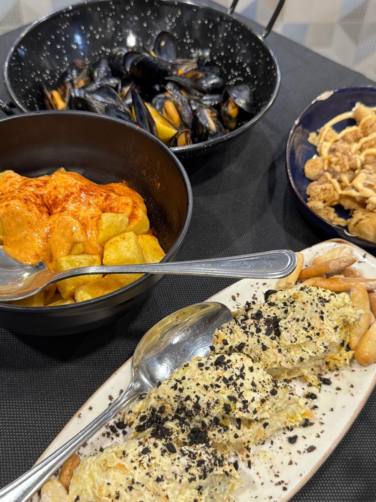 Mejillones, patatas bravas, ensaladilla rusa con picatostes y calamares sobre la mesa