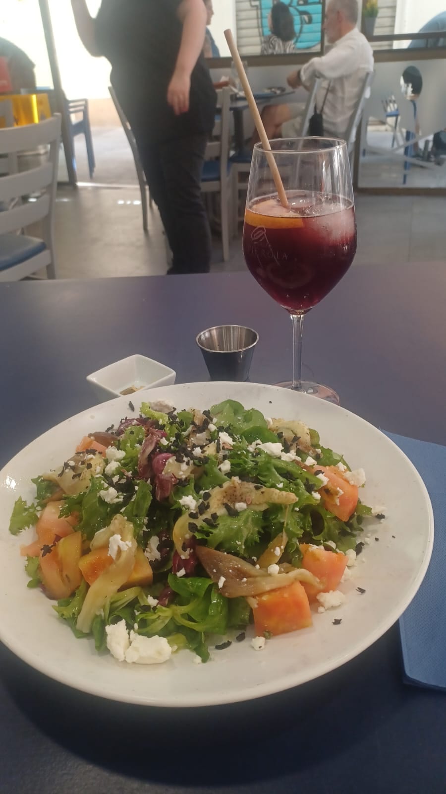 Ensalada de hojas con tomate, queso feta y berenjena, junto a una sangría