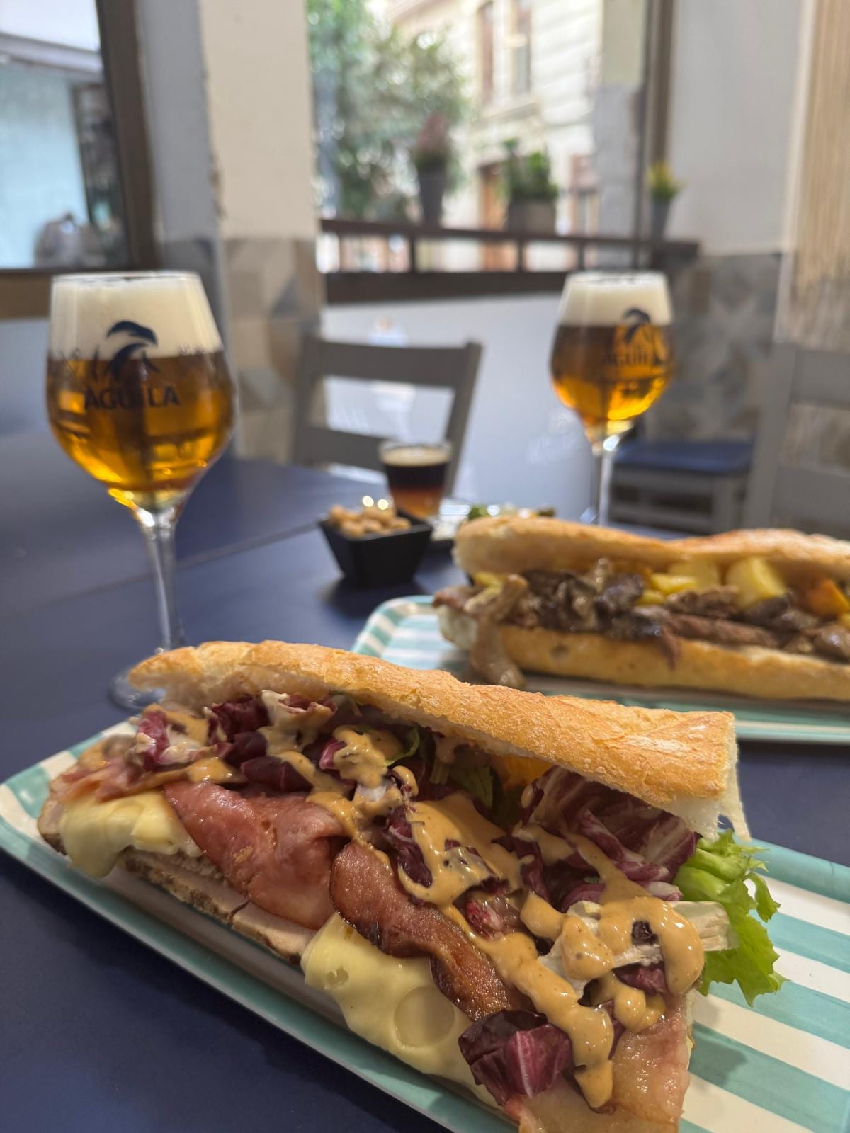 Dos bocadillos con cerveza Águila en copa sobre bandejas a rayas turquesa